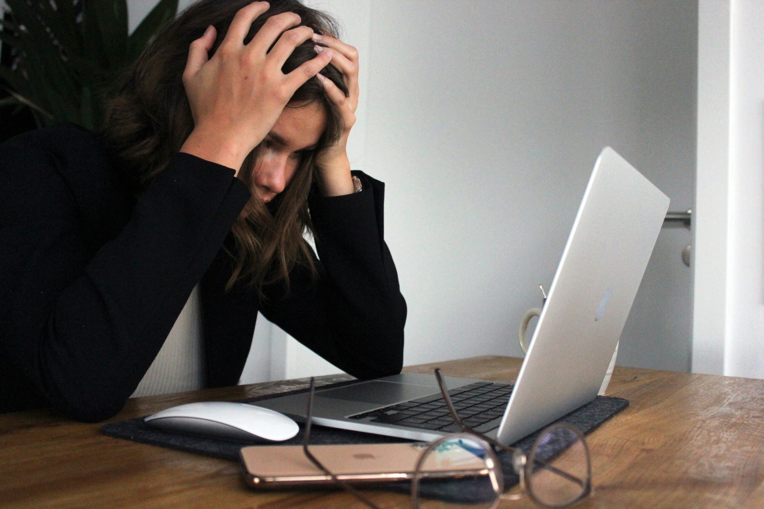 woman sat at a desk with her head in her hands in front of a laptop. Image is used to represent the burnout cycle.