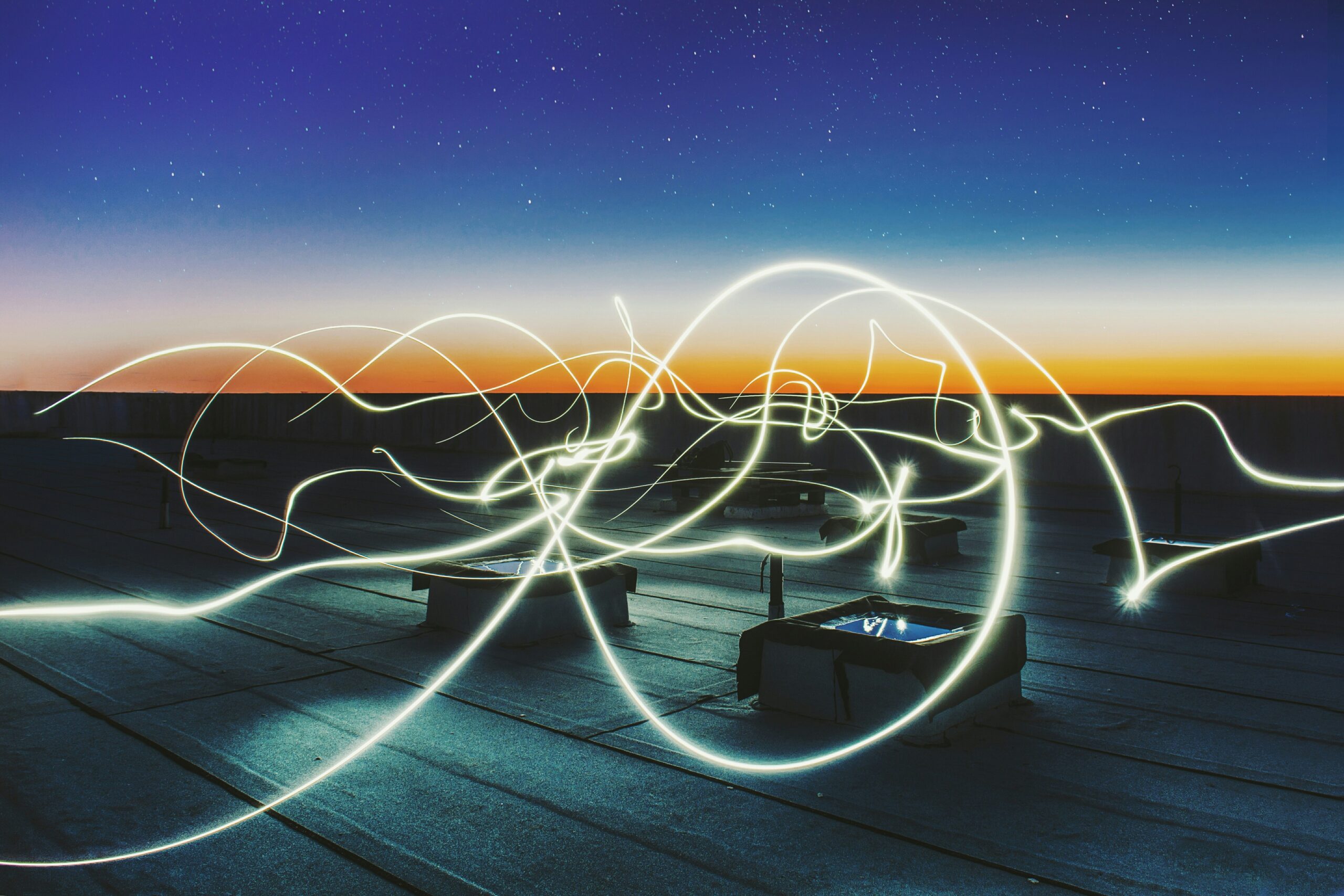 Light trails symbolising invisible energy leaks against a rooftop at dusk, representing the unseen ways professionals lose energy throughout the workday.